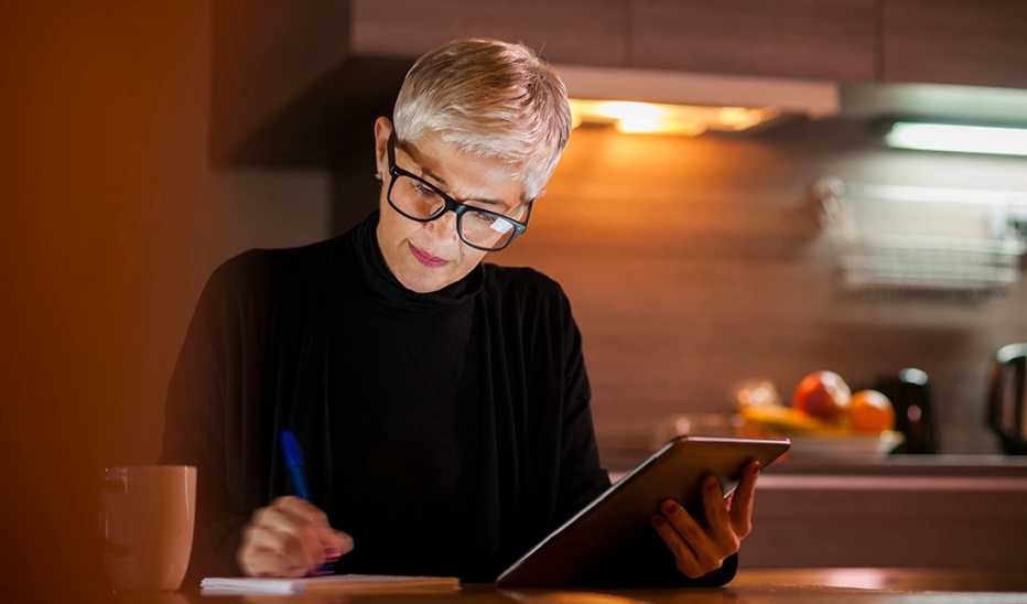 A woman working on a tablet while writing in a notebook