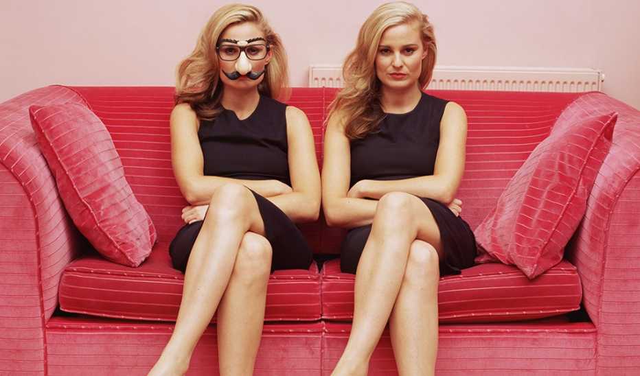 Two similar-looking women on a couch with one wearing a comedy disguise