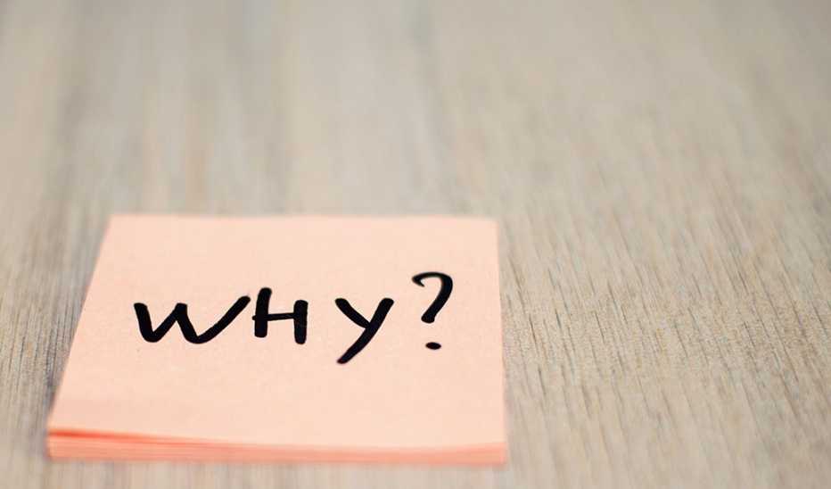 A pad of pink sticky notes on a table with the word "why" written on the top note