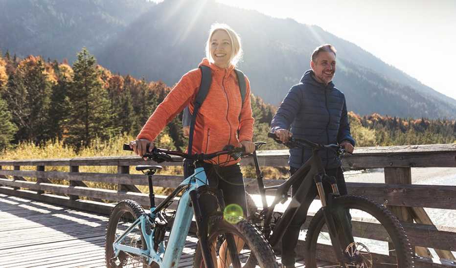 A man and woman walking across a bridge with their bikes in the mountains