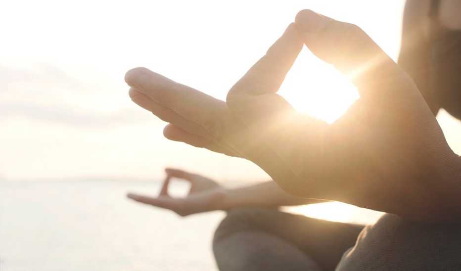 A close up of the hands of a person doing yoga by the sea