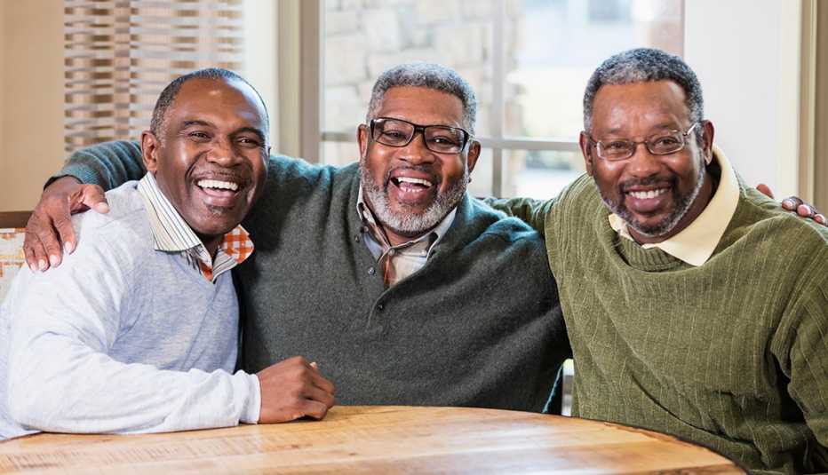 Three smiling men sitting at a table with their arms around each other's shoulders