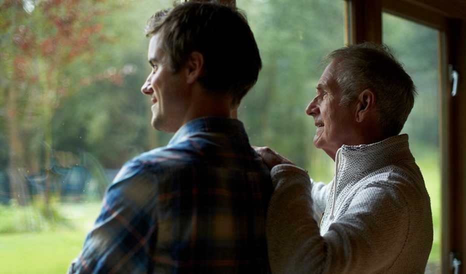 Two men looking out the window of a cottage in the woods