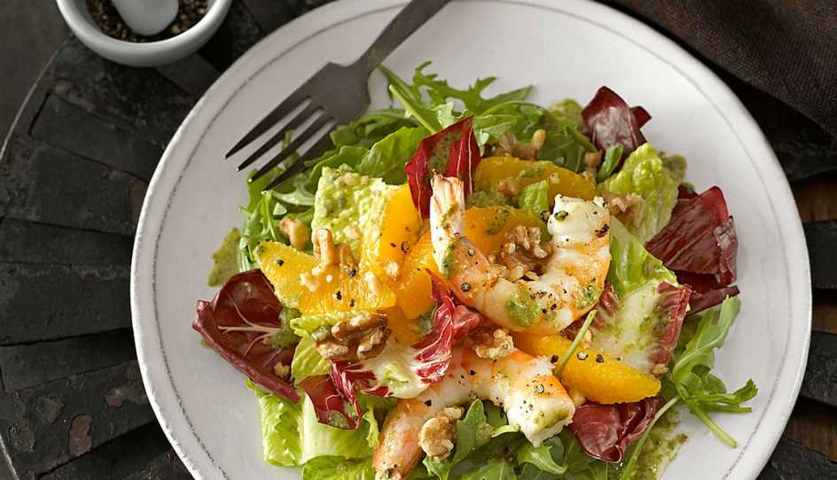 A close-up view of orange and black pepper shrimp salad on a plate