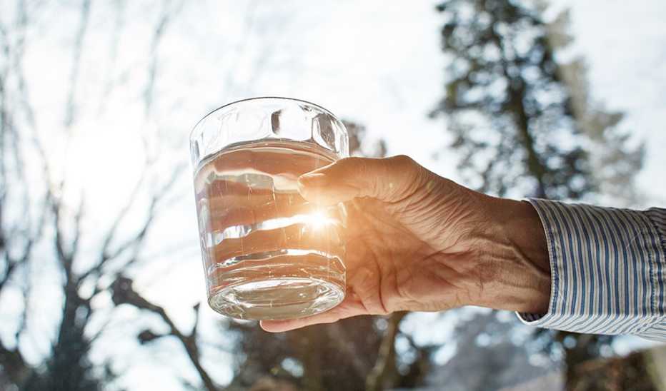 A close up of a hand holding up a glass of water outside