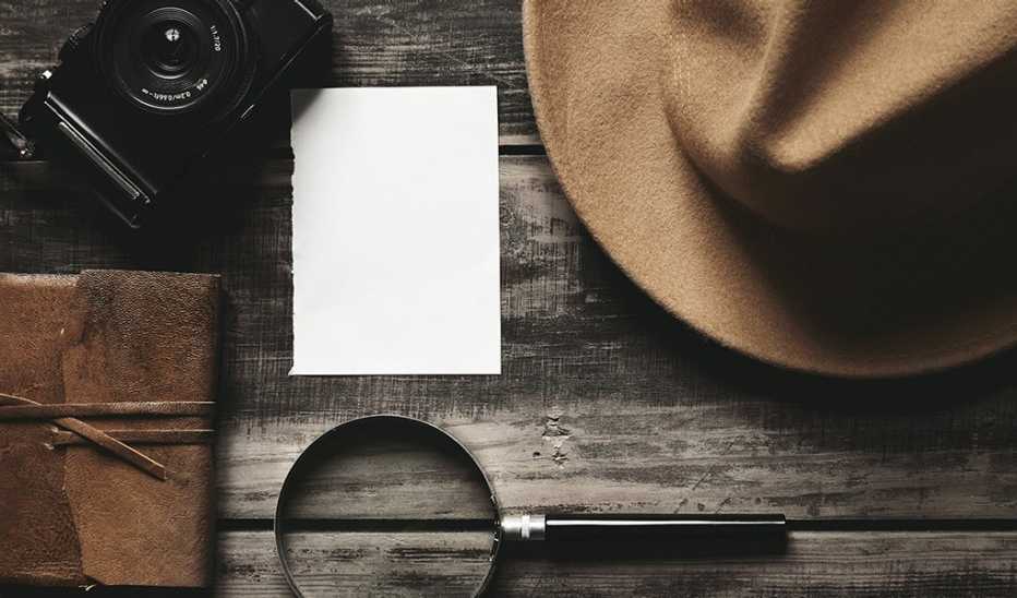 A magnifying glass, camera and hat on a wooden table