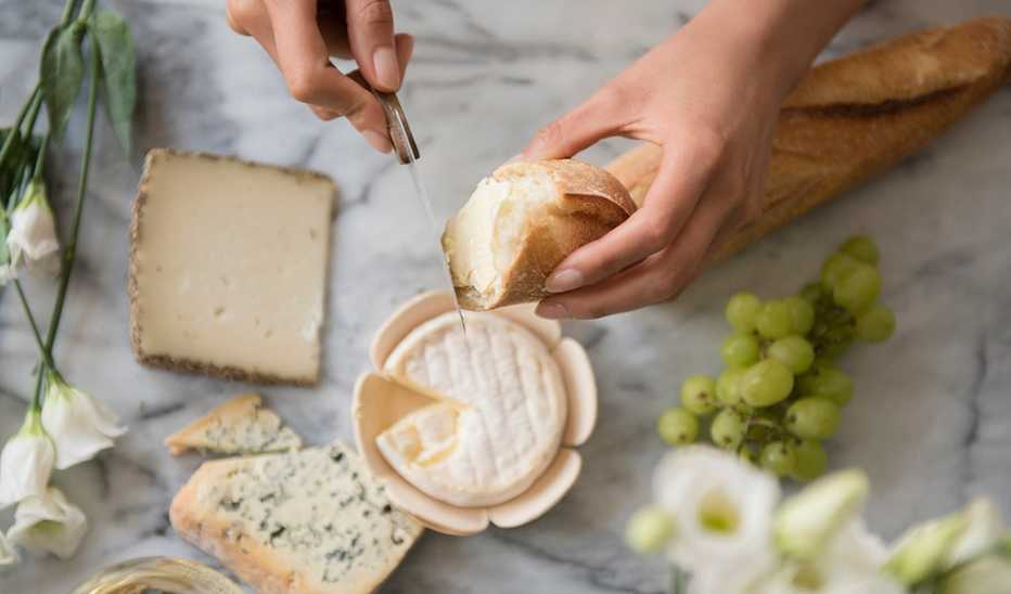 Hands of a person using a knife to spread cheese on bread