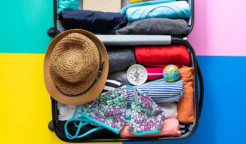 A suitcase packed tightly with a swimsuit, beach hat and compass on the top