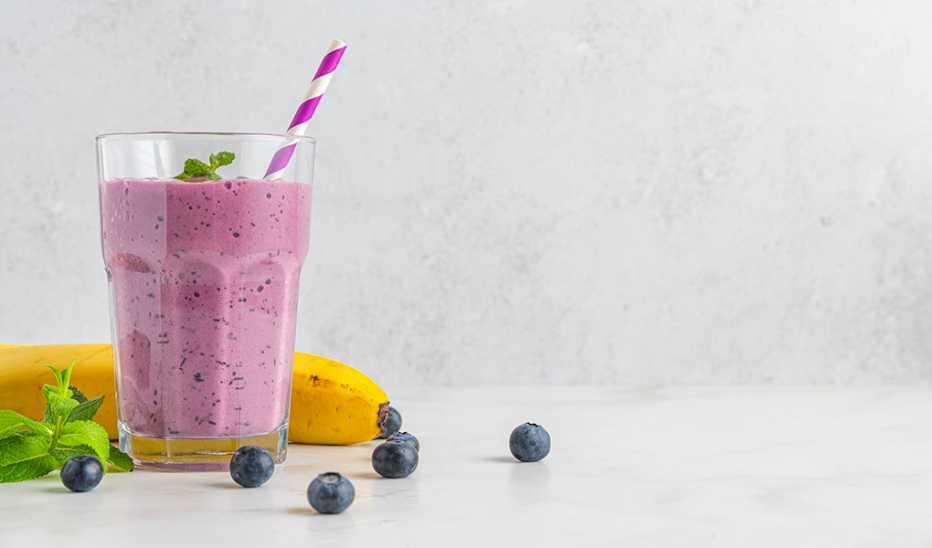 A blueberry and banana smoothie with a banana and blueberries beside it