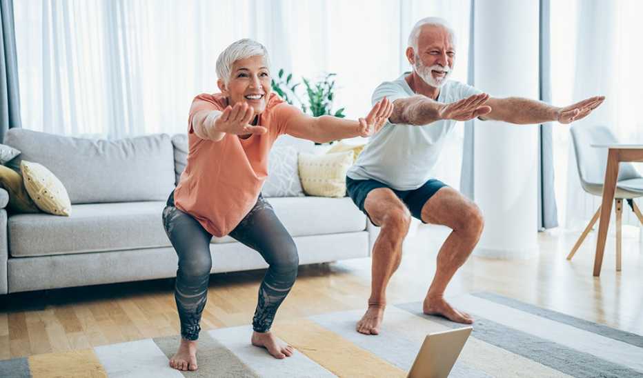 A man and woman doing air squats in the living room of a home