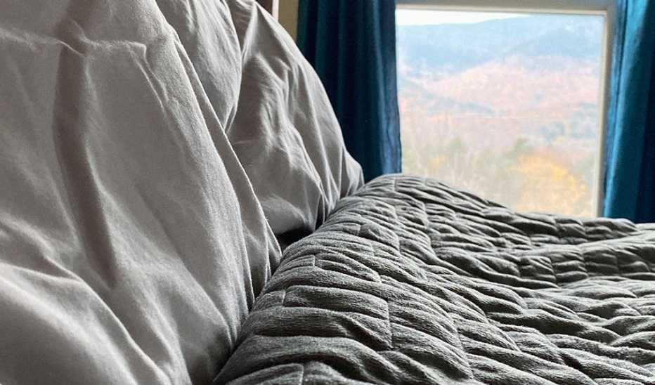 A weighted blanket on a bed with a window in the background