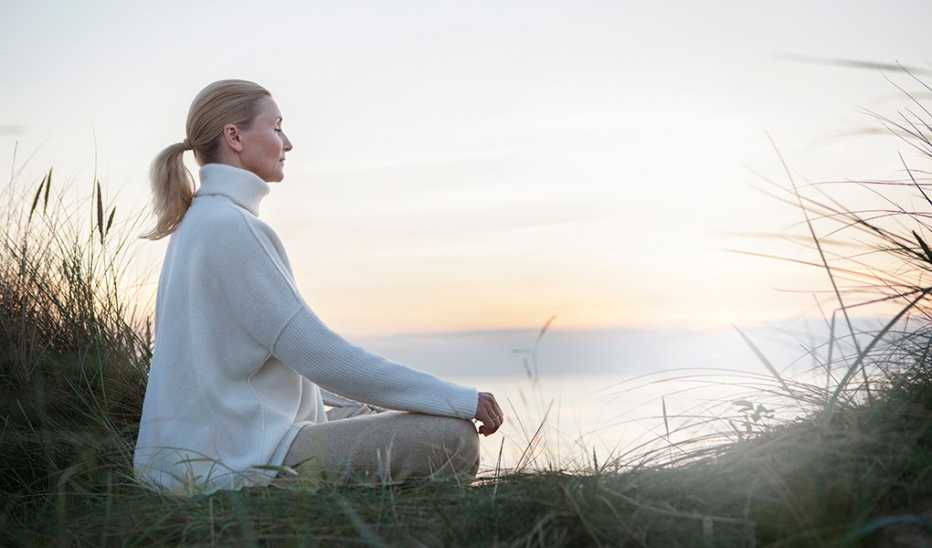 A woman meditating on a beach at sunset