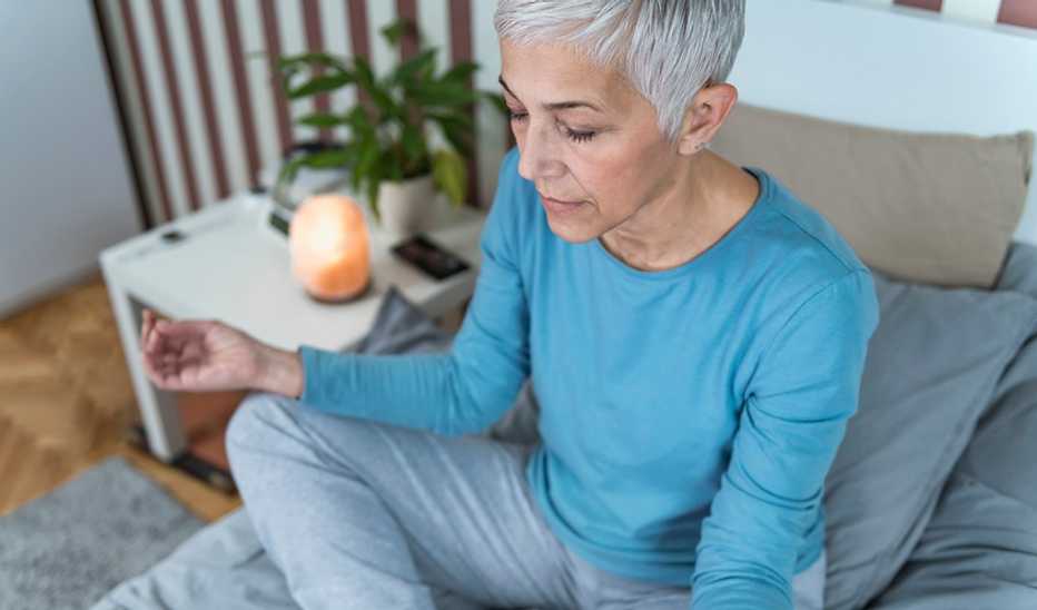 A woman meditating in a lotus position on her bed