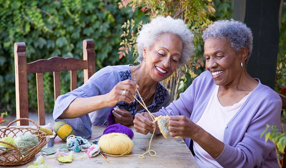 Two women knitting together at a table outside
