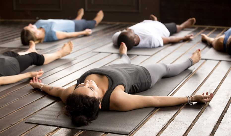 A group of people are lying on mats doing the savasana yoga pose