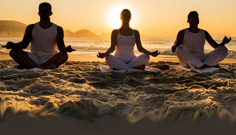 Three people meditating on the beach at sunset