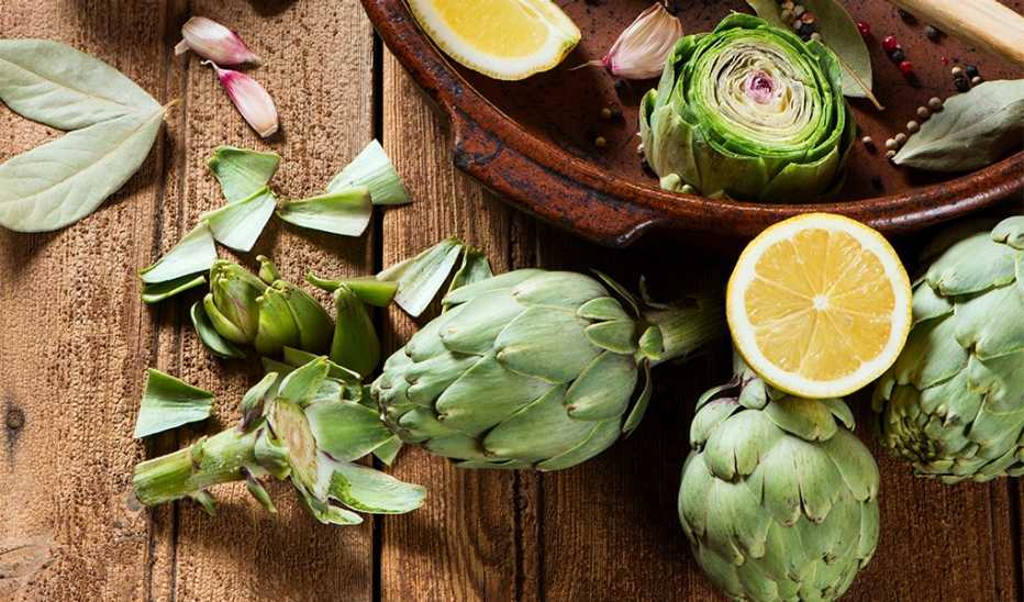 A close-up view of raw artichokes with olive oil and spices on a wooden background