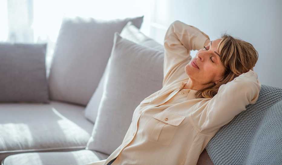 A woman relaxing on the couch with her eyes closed and her hands behind her head