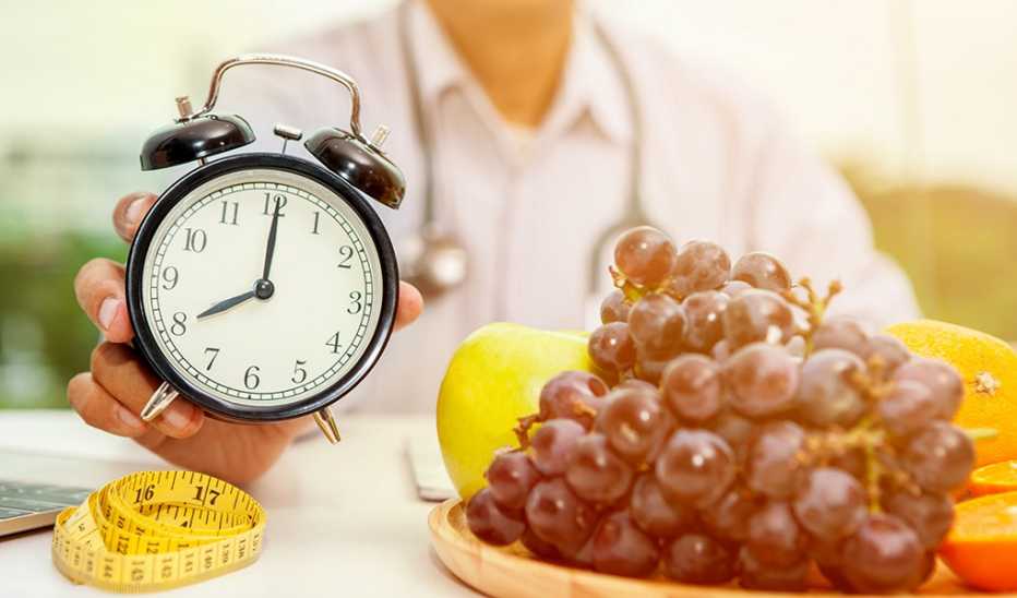 A person holding an alarm clock with fruits in front of him