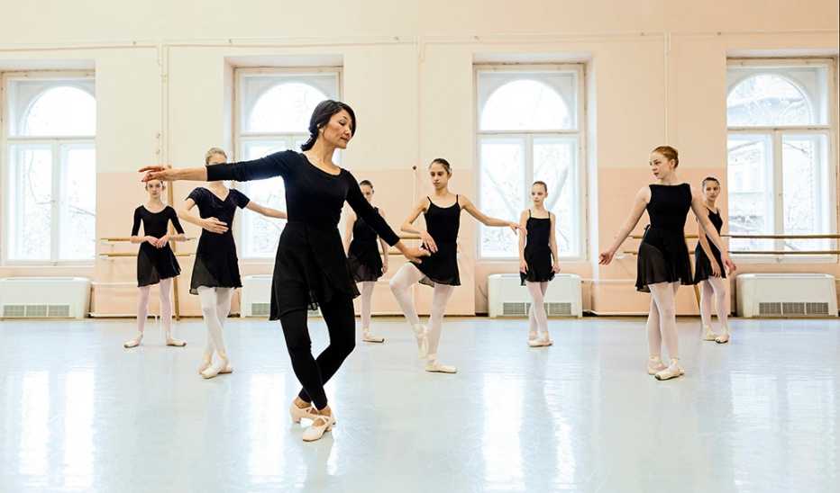 Ballerinas in dance studio practicing with teacher showing poses