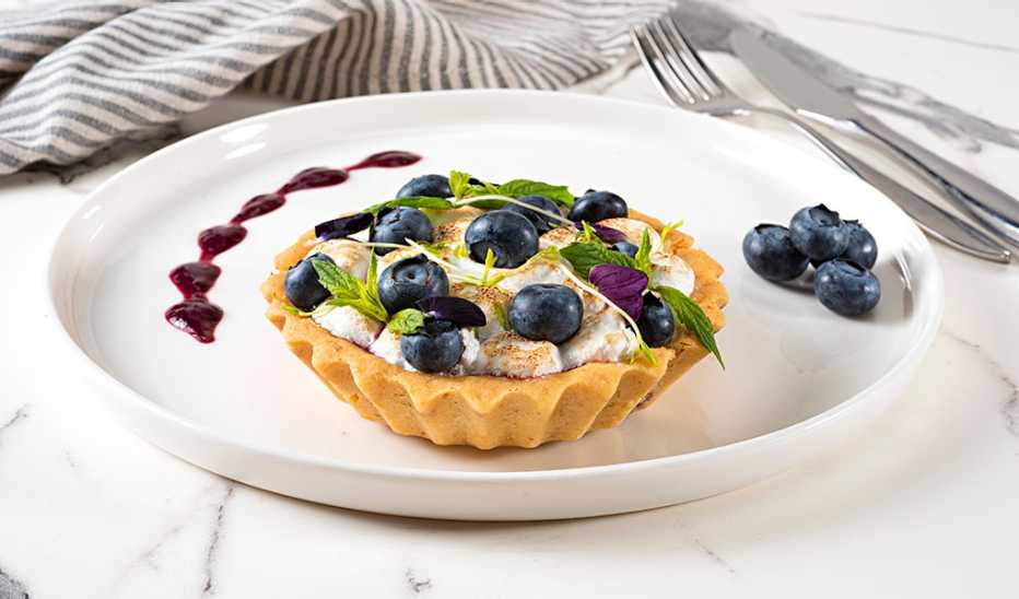 An up-close view of a lemon and blueberry tartlet on a plate