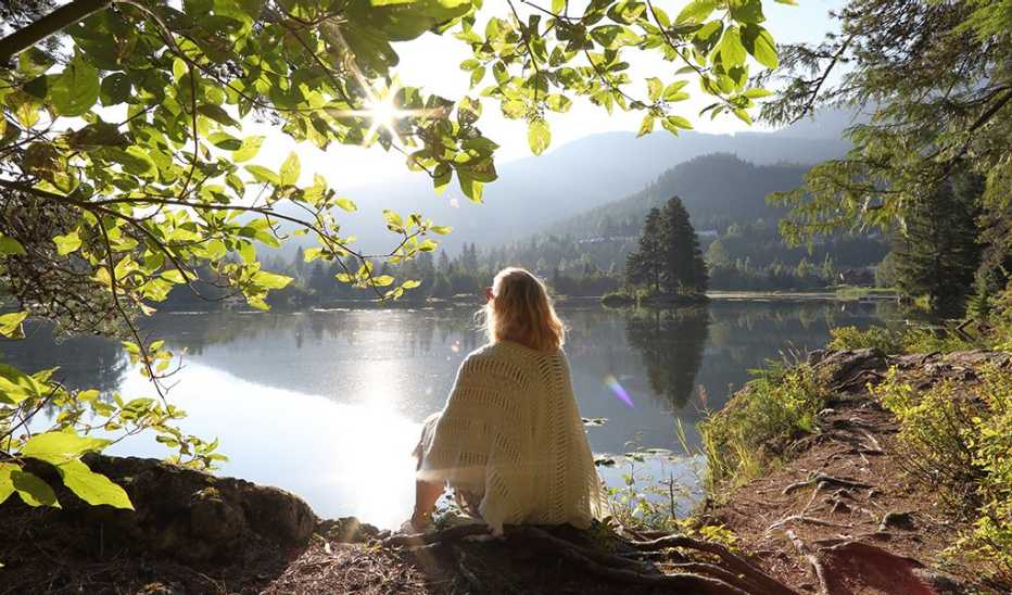 A woman sitting by a lake with mountains in the distance