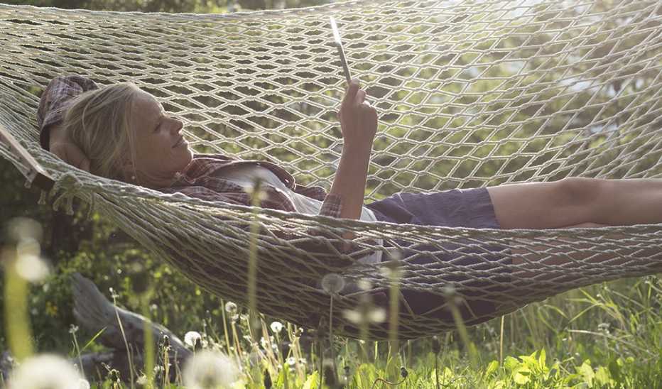 A woman looking at a tablet as she lies in a hammock