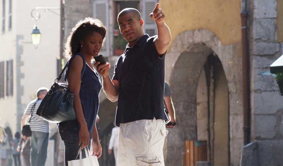 A man pointing in a direction as a woman looks at his phone