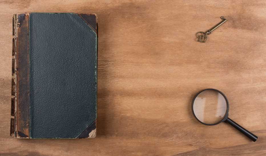 An old book, key and magnifying glass laying on a wooden background