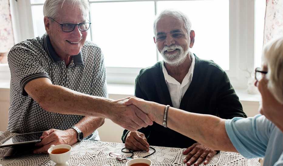 A man and woman shaking hands at the table while another man smiles