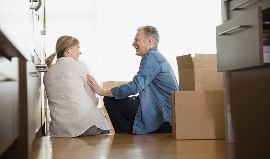 A man and woman sitting on the floor and laughing next to moving boxes