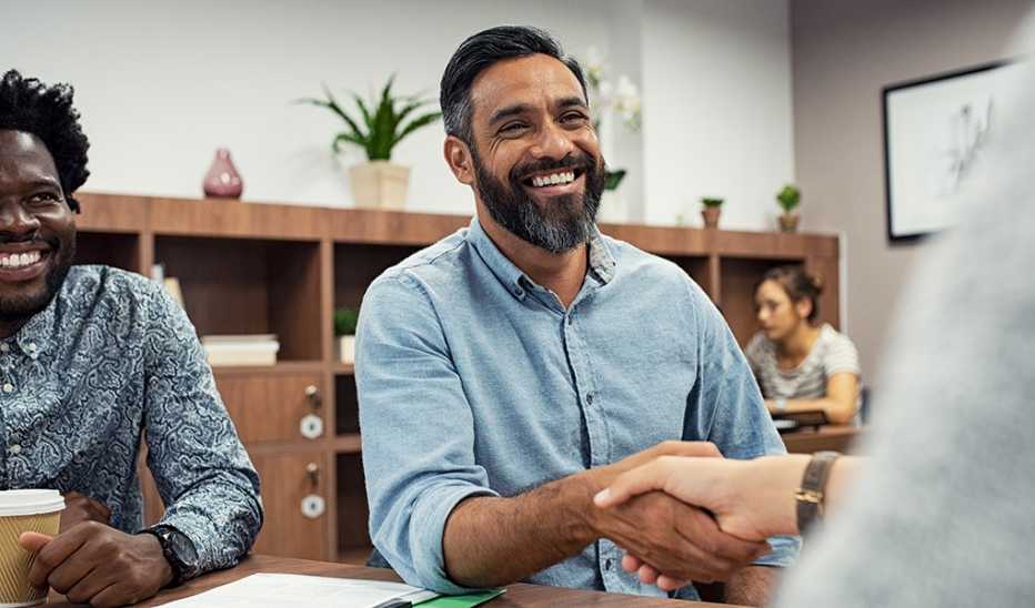Two men are smiling as one of them shakes the hand of another person