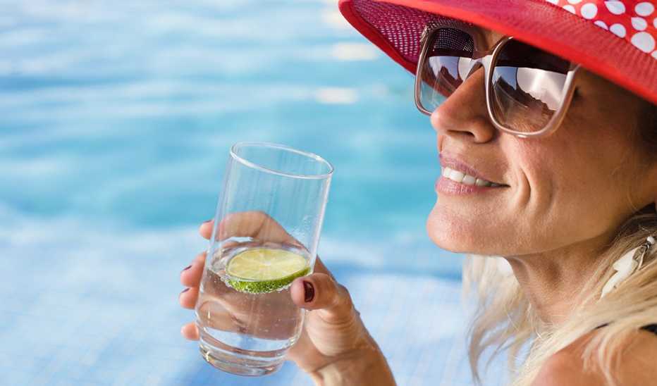 A woman drinking a glass of water by a pool