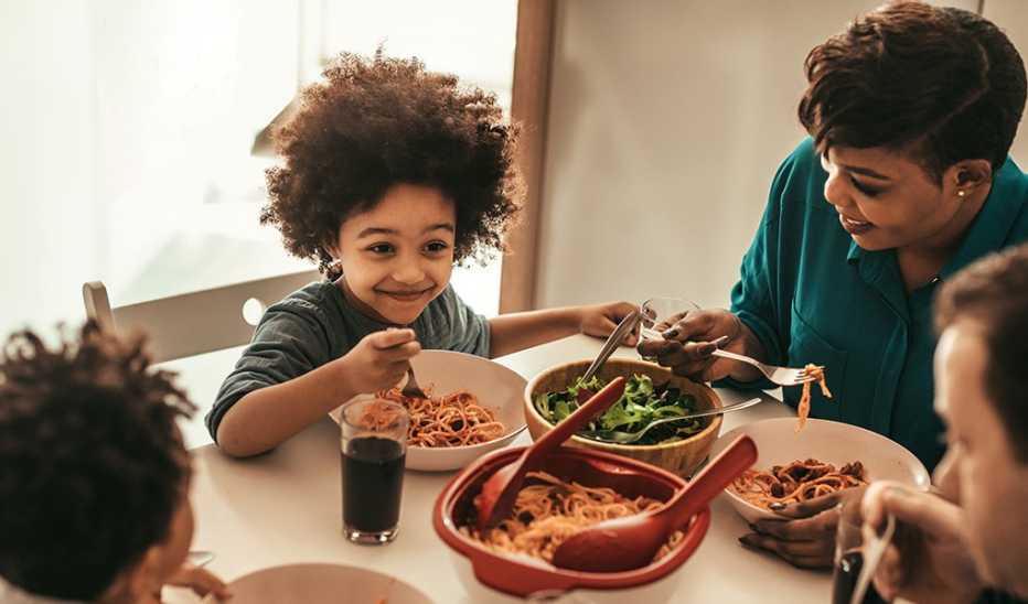 A young child is smiling as they eat lunch at a table with their family