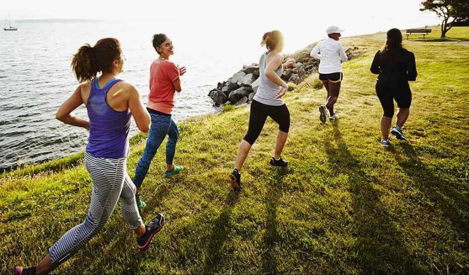 A group of women running on grass by a body of water