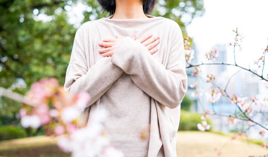 A woman stands with her arms crossed next to cherry blossoms