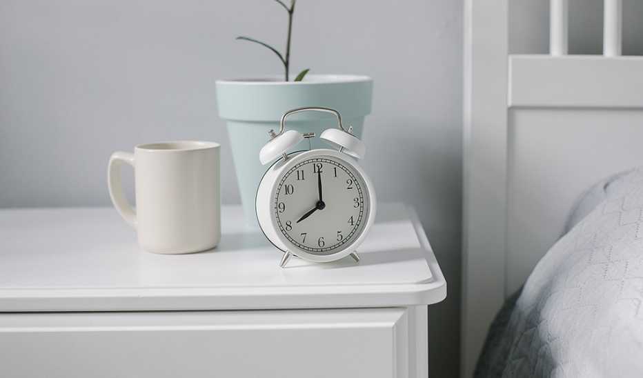 Having a regular sleep-wake schedule is related to better brain health A white alarm clock on a nightstand by a bed