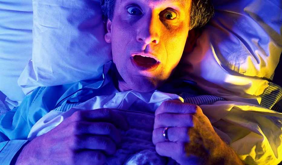 A man lying wide eyed in a bed