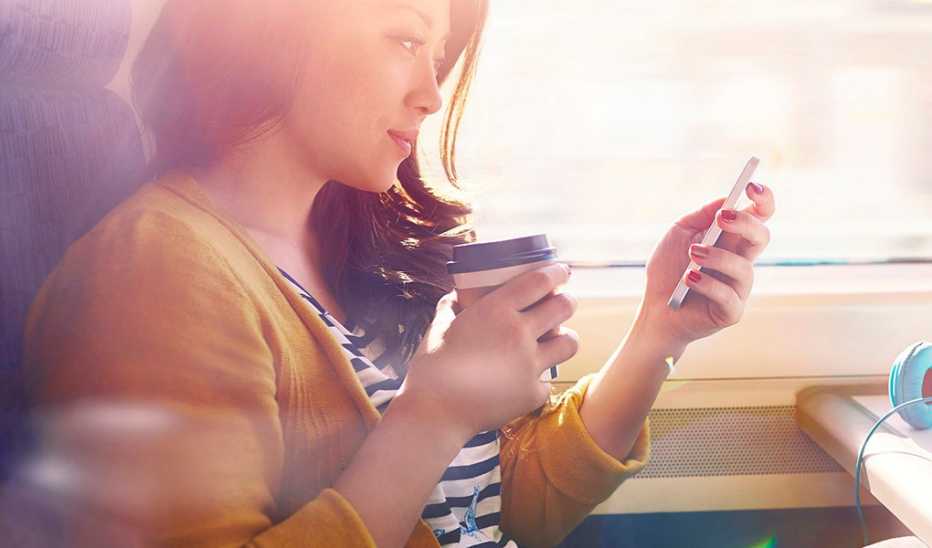 A woman looking at her phone in one hand with coffee in the other hand
