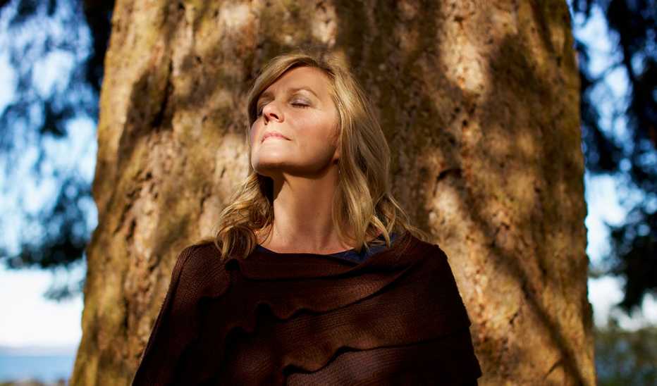 A woman with her eyes closed standing by a tree