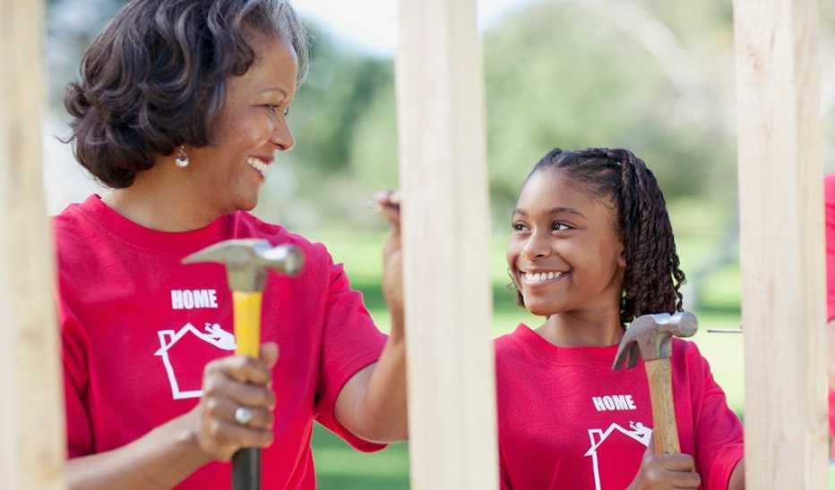 A woman and girl hammering nails on a house they're building