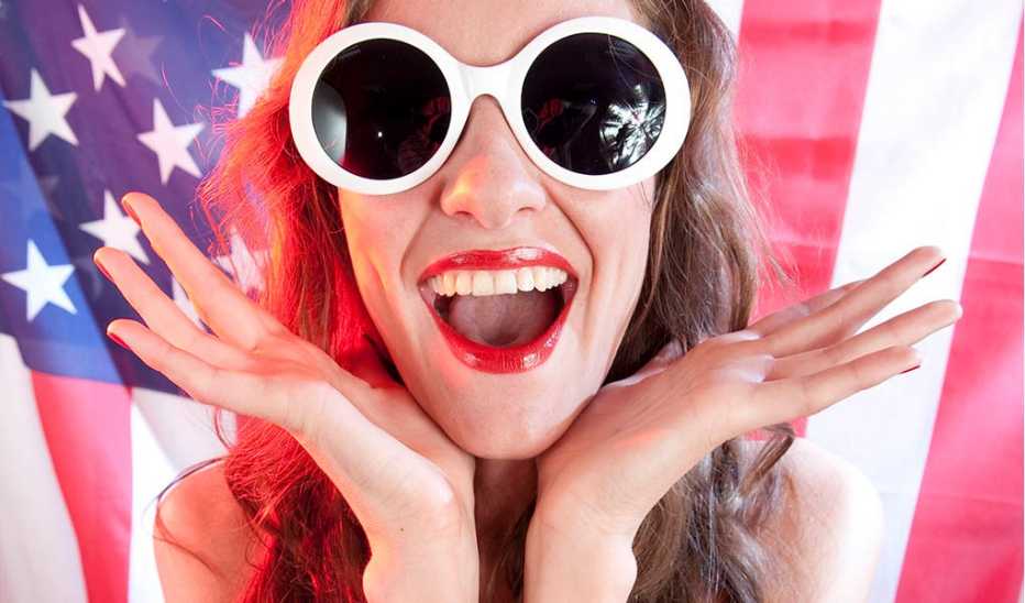 A woman wearing sunglasses smiling in front of an American flag