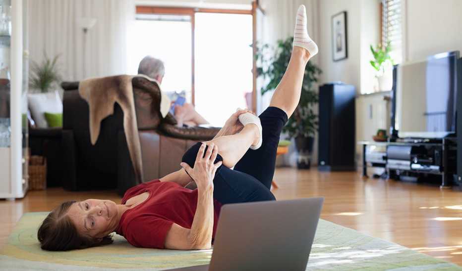 A woman stretching on the floor at home with a laptop in front of her