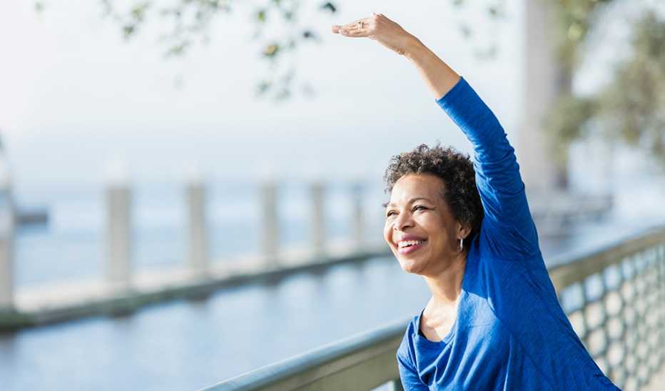 A woman stretching her arm over her head along a waterfront