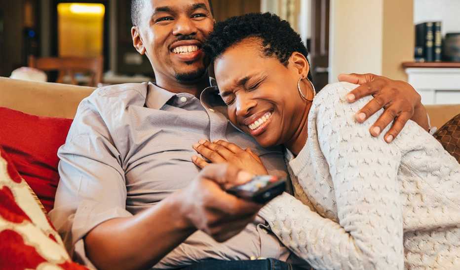 A man and woman smiling and watching TV together on the couch