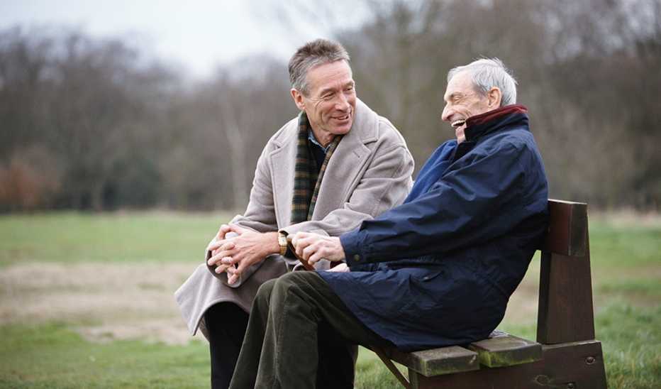 Two men smiling and talking to each other on a park bench