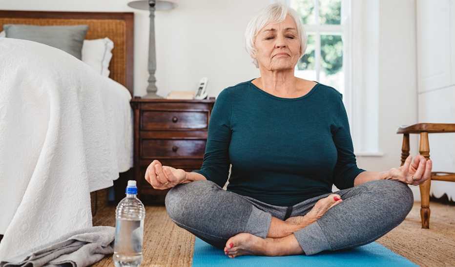 A woman doing yoga in a lotus pose by a bed