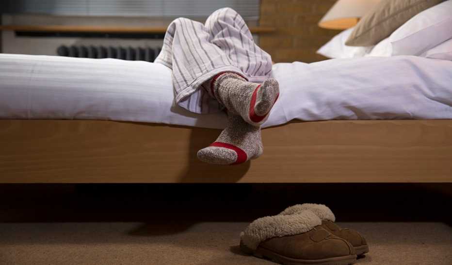 The legs and feet of a person in pajamas hanging over the edge of a bed