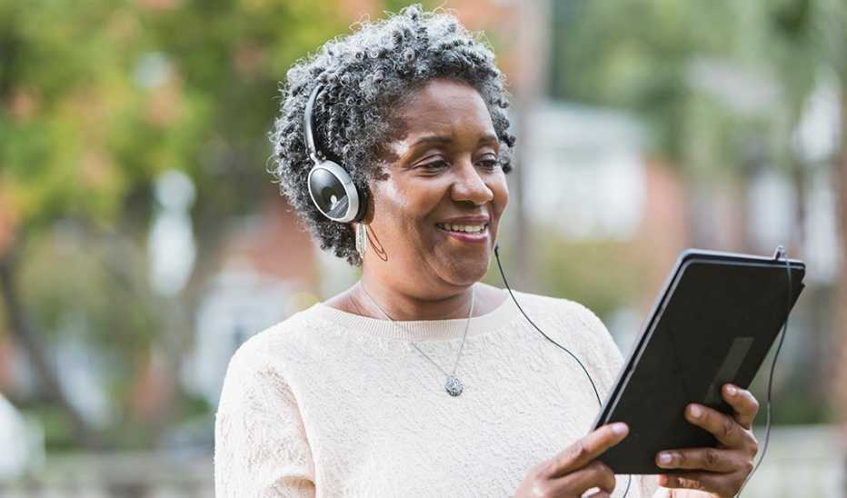 A woman wearing headphones listening to something on a tablet while outside