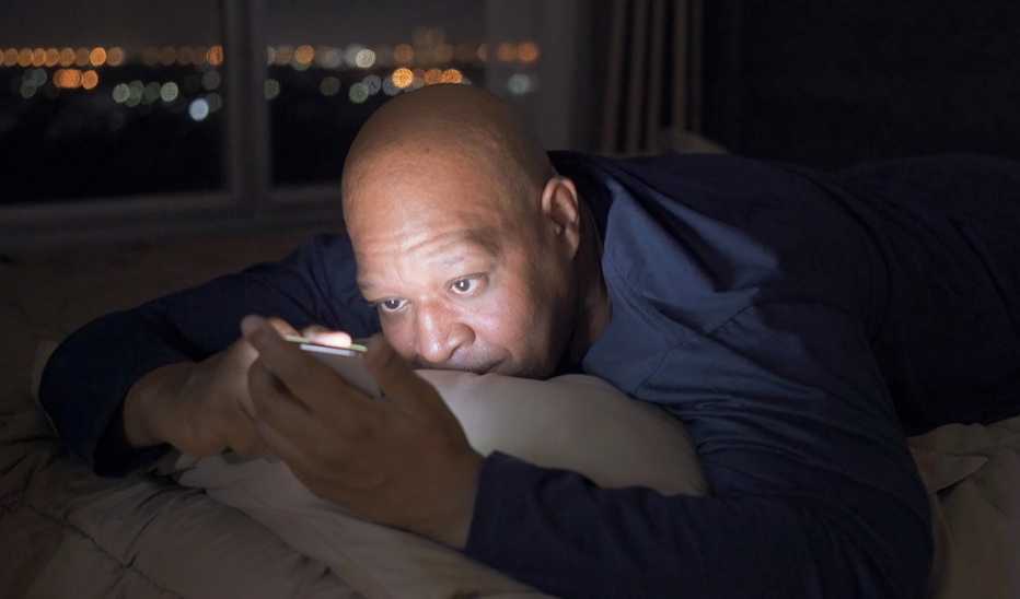 A man using a smartphone in bed at night